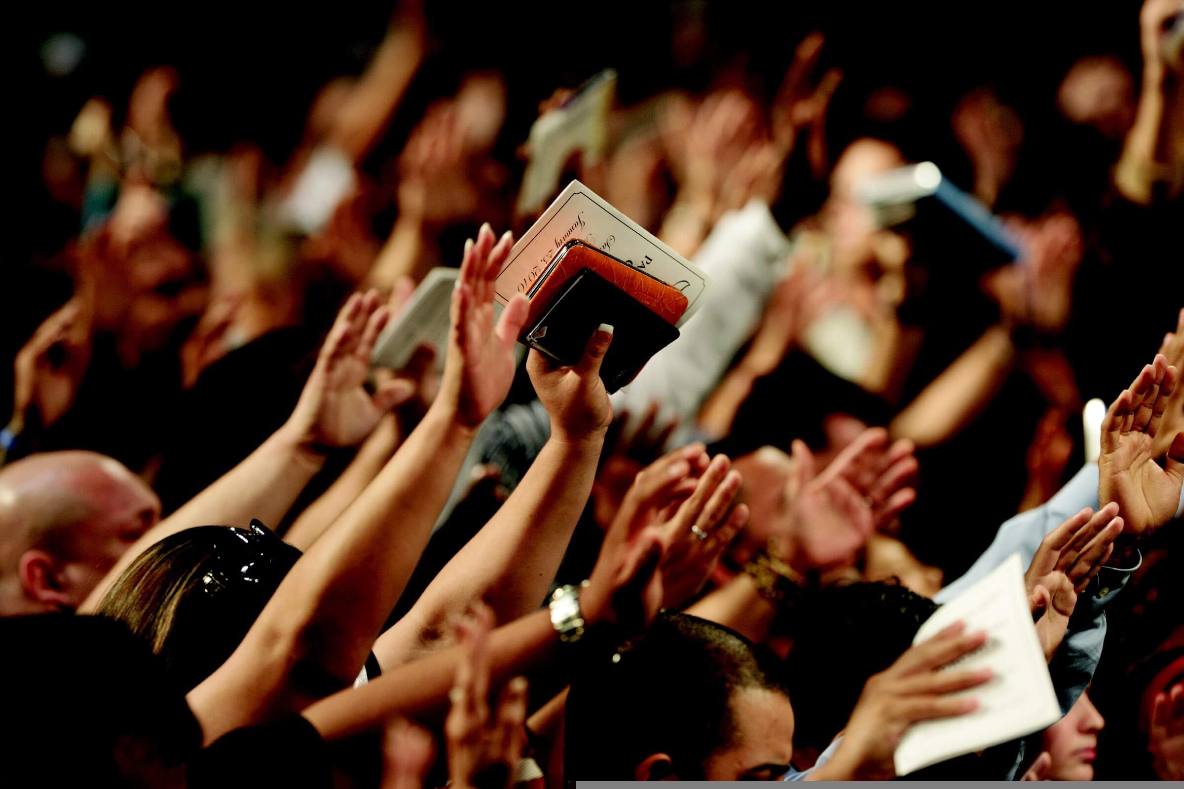 A congregation with hands raised in worship, gathered in shared praise and prayer